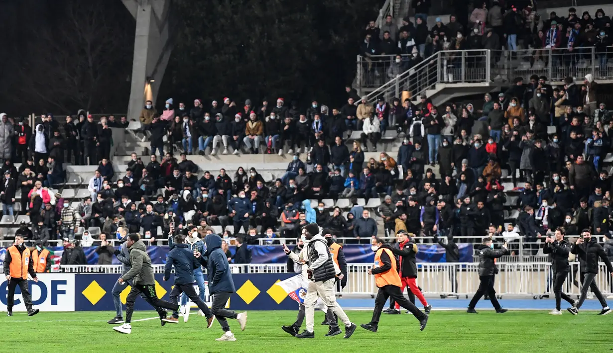 Suporter berlarian di lapangan pada babak pertama pertandingan 64 besar Piala Prancis antara Paris FC dan Olympique Lyon di stadion Charlety, Paris, Jumat (17/12/2021). Laga Paris FC dan Olympique Lyon dihentikan setelah penonton rusuh di stadion. (Bertrand GUAY/AFP)
