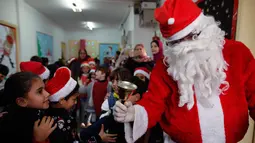 Seorang pria berpakaian seperti Santa Claus menyambut kedatangan anak-anak  saat perayaan menyambut Hari Natal di Sekolah Amerika di Kota Gaza (20/12).  (AFP Photo/Mohammed Abed)