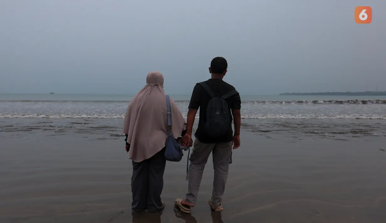 Yanti, istri jurnalis foto Merdeka.com Arie Basuki, bersama putranya Bintang berdiri menatap perairan Selat Sunda sambil memanjatkan doa dalam prosesi tabur bunga di pantai dekat Dermaga Pegedongan, Banten, Jumat (18/9/2026). Doa tersebut dipanjatkan sebagai bentuk harapan agar Arie Basuki dan tujuh penumpang Arupadhatu 1 lainnya segera ditemukan. (KLY/Budy Santoso)