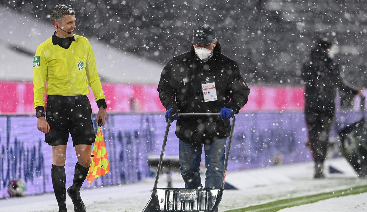 Seorang pekerja membersihkan lapisan salju dari permukaan lapangan dalam laga lanjutan Liga Jerman 2020/21 pekan ke-21 antara Bayern Munich melawan Arminia Bielefeld di Allianz Arena, Munich, Senin (15/2/2021). Bayern Munich bermain imbang 3-3 dengan Arminia Bielefeld. (AFP/Christof Stache/Pool)