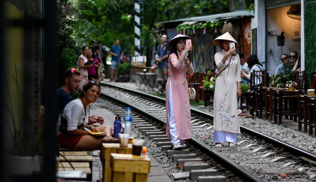 Foto pada 8 Juni 2019 menunjukkan uris mengenakan kostum tradisional Vietnam berswafoto di tengah jalur kereta api populer di Hanoi. Di ibu kota Vietnam tersebut rel-rel kereta yang berada di permukiman padat penduduk dijadikan destinasi wisata selfie. (Photo by Manan VATSYAYANA / AFP)
