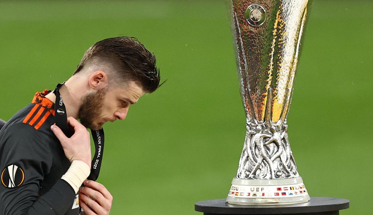 Reaksi kecewa kiper Manchester United, David de Gea saat berjalan melewati trofi Liga Europa 2020/2021 setelah dikalahkan Villarreal CF di Gdansk Stadium, Gdansk, 26 Mei 2021. Meskipun begitu, De Gea pernah mempersembahkan satu trofi Liga Europa untuk MU pada 2016/2017. Kala itu Setan Merah berhasil menang dengan skor 2-0 atas Ajax Amsterdam. (AFP/Pool/Maja Hitij)