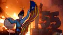 Sebuah karakter yang mewakili mantan presiden Catalan, Carles Puigdemont sedang memegang bendera Catalonia dibakar saat festival tradisional Fallas di Valencia, Spanyol (19/3). (AP/Alberto Saiz)