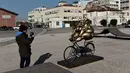 Seorang pria mengambil gambar patung karya seniman China Xu Hongfei di Thessaloniki, Yunani, Rabu (19/12). Sebanyak 15 patung karya Xu Hongfei menghiasi tepi pantai Thessaloniki. (Sakis Mitrolidis/AFP)