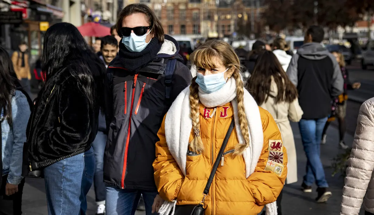 Orang-orang dengan masker melintasi jalan di pusat kota Amsterdam, Belanda, Rabu (3/11/2021). Dengan aturan terbaru, pemerintah Belanda mewajibkan penggunaan masker di ruang-ruang publik seperti tempat perbelanjaan, perpustakaan, salon, stasiun kereta, hingga rumah sakit. (Ramon van Flymen/ANP/AFP)