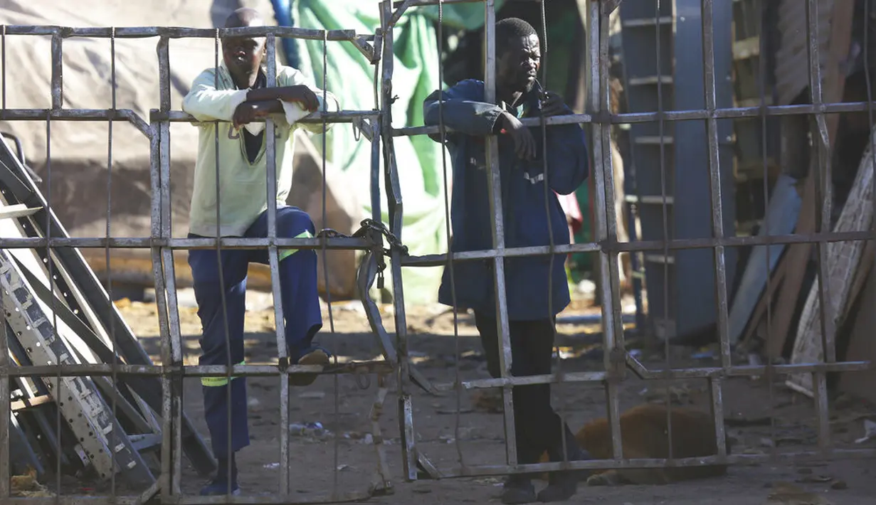 Pekerja perusahaan besi tua melihat dari balik pagar di Harare, Zimbabwe, Selasa (6/1/2021). Menanggapi meningkatnya infeksi COVID-19, Zimbabwe telah memberlakukan kembali jam malam, melarang pertemuan publik, dan menangguhkan pembukaan sekolah tanpa batas waktu. (AP Photo/Tsvangirayi Mukwazhi)