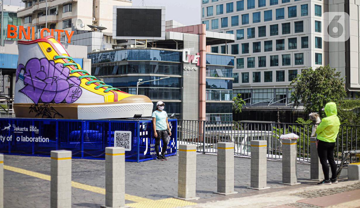 Warga berfoto di depan Tugu Sepatu, Sudirman, Jakarta, Minggu (19/9/2021). Tugu Sepatu menjadi sasaran pencoretan dengan semprotan aerosol oleh orang tak dikenal sehari usai diresmikan pada 17 September 2021. (Liputan6.com/Faizal Fanani)