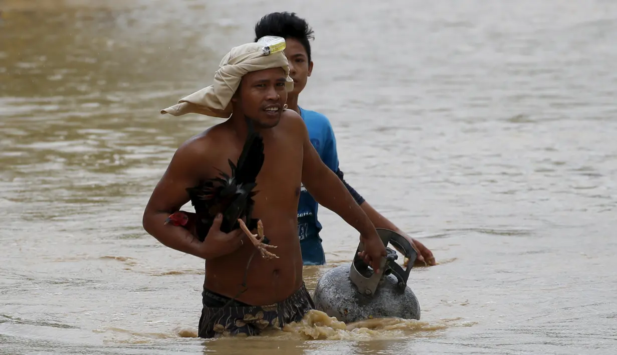 Seorang warga tampak membawa tabung gas dan hewan peliharaanya melewati jalanan yang banjir pasca bencana badai topan Koppu di Nueva Ecija,  Filipina, Senin (19/10/2015). Badai terjadi pada Minggu pagi waktu setempat. (REUTERS/Erik De Castro)