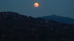 Bulan Purnama Super Pink terlihat di atas lingkungan Petare di Caracas, Venezuela, pada Senin (26/4/2021). Super Pink Moon merupakan fenomena alam ketika posisi bulan purnama berada terdekat dengan bumi. (Federico Parra / AFP)