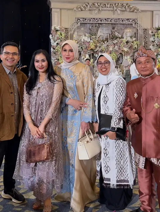 Iis Dahlia mengenakan tunik ungu berbordir dipadukan bawahan batik dan membawa hand bag coklatnya. [@marinizumarnisreal]