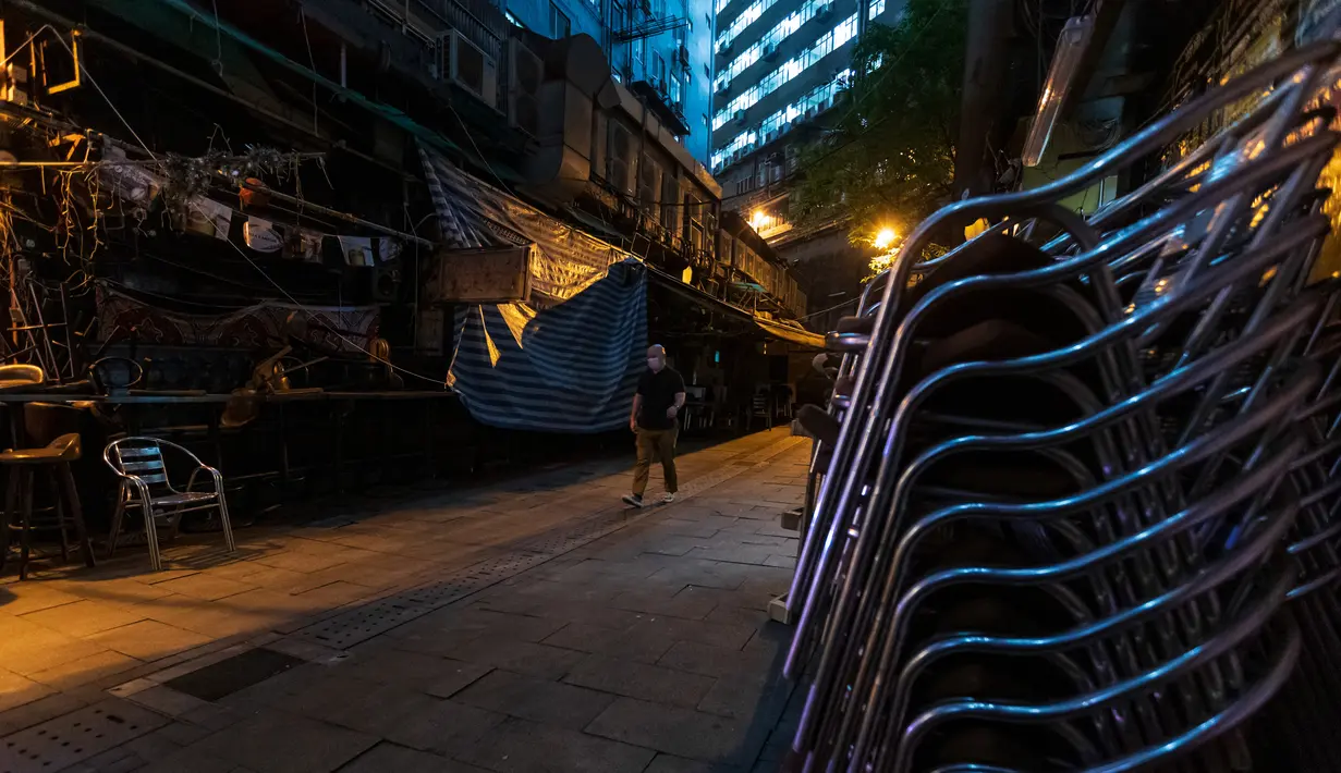 Seorang pria mengenakan masker pelindung melintas di jalanan sepi di kawasan hiburan malam Lan Kwai Fong, Hong Kong (5/5/2020). Kebijakan pemerintah Hong Kong itu membuat gemerlap hiburan malam di Lan Kwai Fong meredup seketika. (AFP/May James)