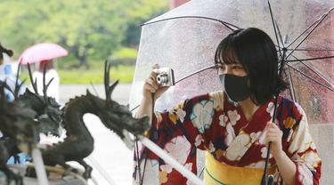 Seorang wanita mengenakan  yukata, pakaian musim panas tradisional Jepang dan masker untuk melindungi diri dari virus corona mengambil foto di lingkungan Asakusa di Tokyo, Jumat (13/8/2021). Yukata adalah jenis kimono yang dibuat dari bahan kain katun tipis tanpa pelapis. (AP Photo/Koji Sasahara)