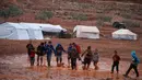 Anak-anak berjalan melewati genangan air hujan di depan tenda di sebuah kamp untuk warga Suriah yang kebanjiran di dekat desa Killi di utara provinsi Idlib barat laut (5/12/2019). (AFP Photo/Aaref Watad)