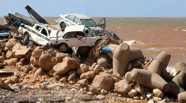 Mobil bertumpuk di atas pemecah gelombang dan puing-puing bangunan yang hancur akibat banjir bandang setelah badai Mediterania "Daniel" menghantam kota Derna di timur Libya, Kamis (14/9/2023). (Abdullah DOMA / AFP)