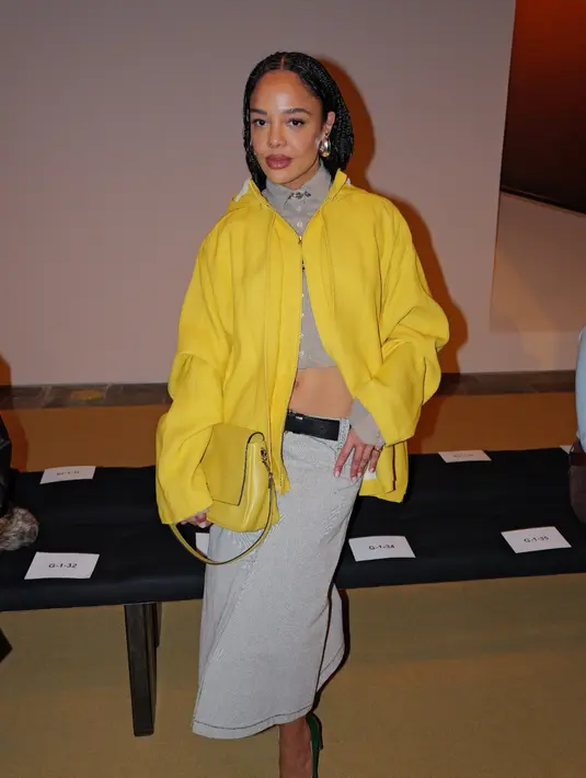Tessa Thompson memilih pendekatan statement dengan waxed yellow jacket yang dipadukan kemeja katun dan rok kanvas. Aksesori seperti kalung barbed wire dan anting Pierced wave memberi kesan edgy namun tetap sophisticated. [dok/toryburch].