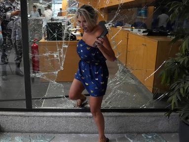 Seorang karyawan bank keluar dari bank melalui jendela yang dirusak oleh penyerang, Beirut, Lebanon, Rabu (14/9/2022). Seorang wanita bersenjata dan belasan aktivis masuk ke cabang bank Beirut mengambil alih $13.000 dari tabungannya yang ditahan oleh bank tersebut. (AP Photo/Hussein Malla)