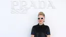 Naomi Watts kenakan blus satin hitam dengan tali leher. Jadi pelengkap rok lipit motif biru toska-hitam, dipadu dengan kacamata cat-eye putih, tas Prada putih, dan loafers hitam [dok. Prada]