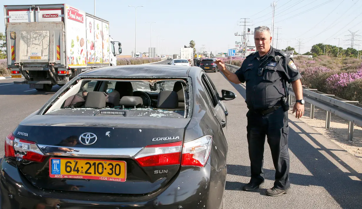 Polisi berdiri dekat mobil yang rusak dalam serangan roket dari Jalur Gaza di Kota Ashdod, Israel, Selasa (12/11/2019). Tewasnya komandan Jihad Islam Baha Abu Al-Ata memicu serangan balasan dari militan Palestina di Gaza. (Jack Guez/AFP)