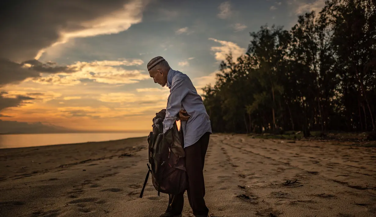 Tengku Mohamad Ali Mansor memeriksa botol kaca di sebuah pantai di desa Mangkuk, Malaysia timur pada 12 September 2020.  Upaya seorang lansia Malaysia untuk membersihkan pantai-pantai negara itu dari kaca-kaca yang terkelupas membuatnya mengumpulkan koleksi ribuan botol. (AFP/Mohd Rasfan)