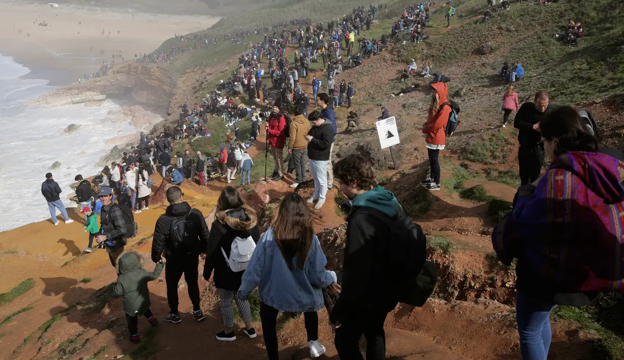 Penonton berkumpul di tebing saat menyaksikan Nazare Tow Surfing Challenge di Praia do Norte atau Pantai Utara, Nazare, Portugal, Selasa (11/2/2020). Hanya peselancar profesional yang boleh bermain ombak di perairan ini. (AP Photo/Armando Franca)