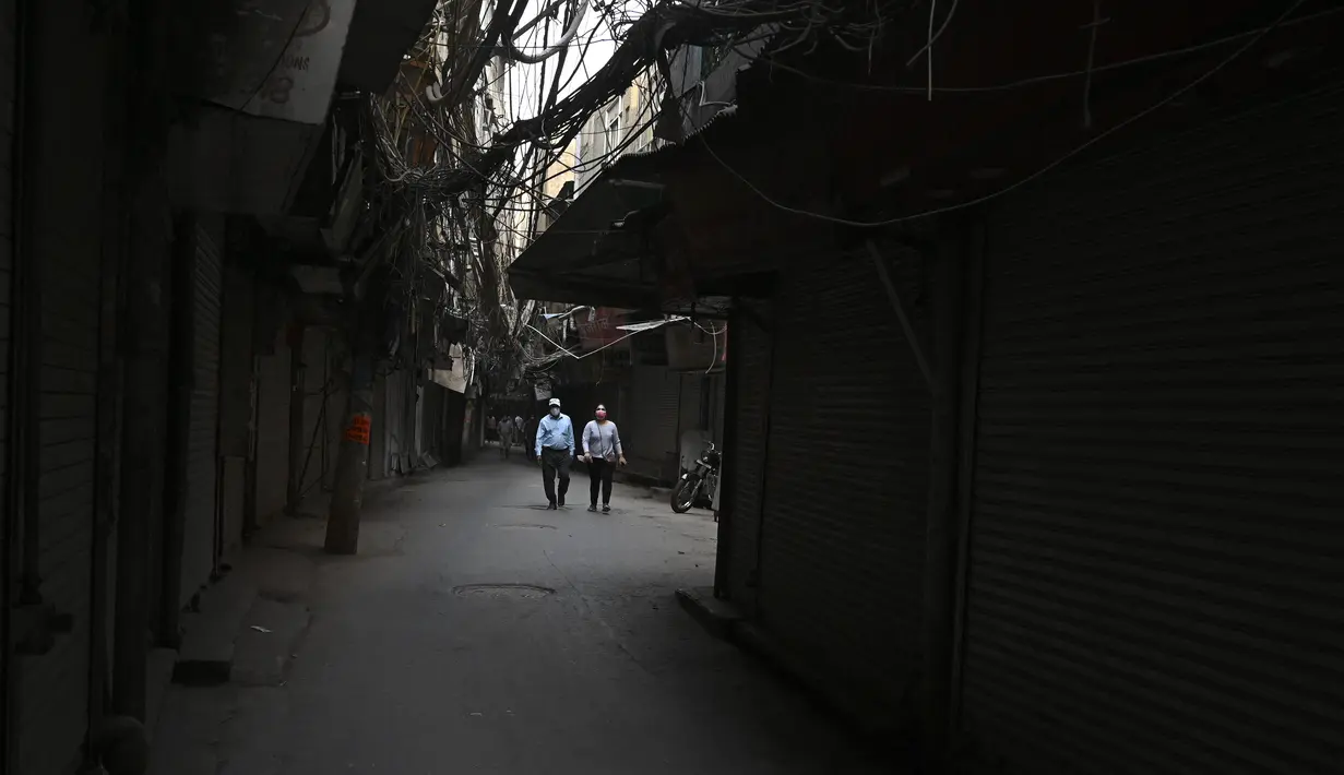 Orang-orang berjalan di sepanjang jalan sepi melewati toko-toko yang tutup di kawasan lama New Delhi ketika ibu kota India melanjutkan lockdown pada Rabu (5/5/2021). Pemerintah India menghadapi seruan lockdown nasional untuk memperlambat gelombang besar infeksi virus corona. (TAUSEEF MUSTAFA/AFP)