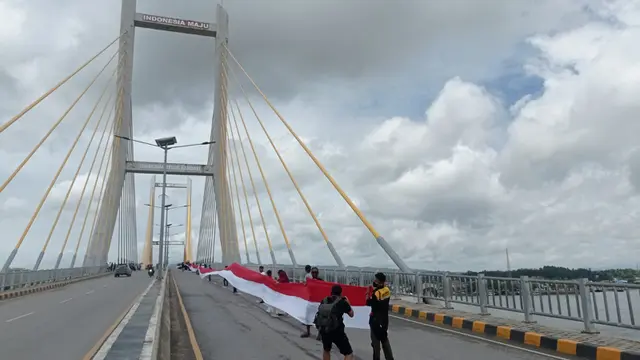 Pemuda memegang Bendera merah putih sepanjang 770 meter, membentang di Teluk Kendari saat perayaan HUT ke-77 RI.(Liputan6.com/Ahmad Akbar Fua)