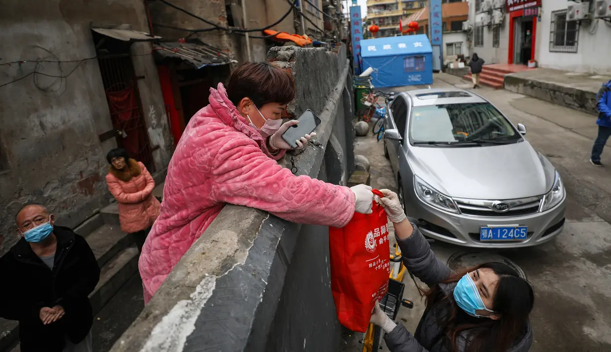 Seorang penduduk menerima sekantong makanan di atas tembok di Wuhan di provinsi Hubei tengah China (3/3/2020). Wuhan merupakan kota di China yang menjadi awal mula wabah virus corona. (AFP/STR)