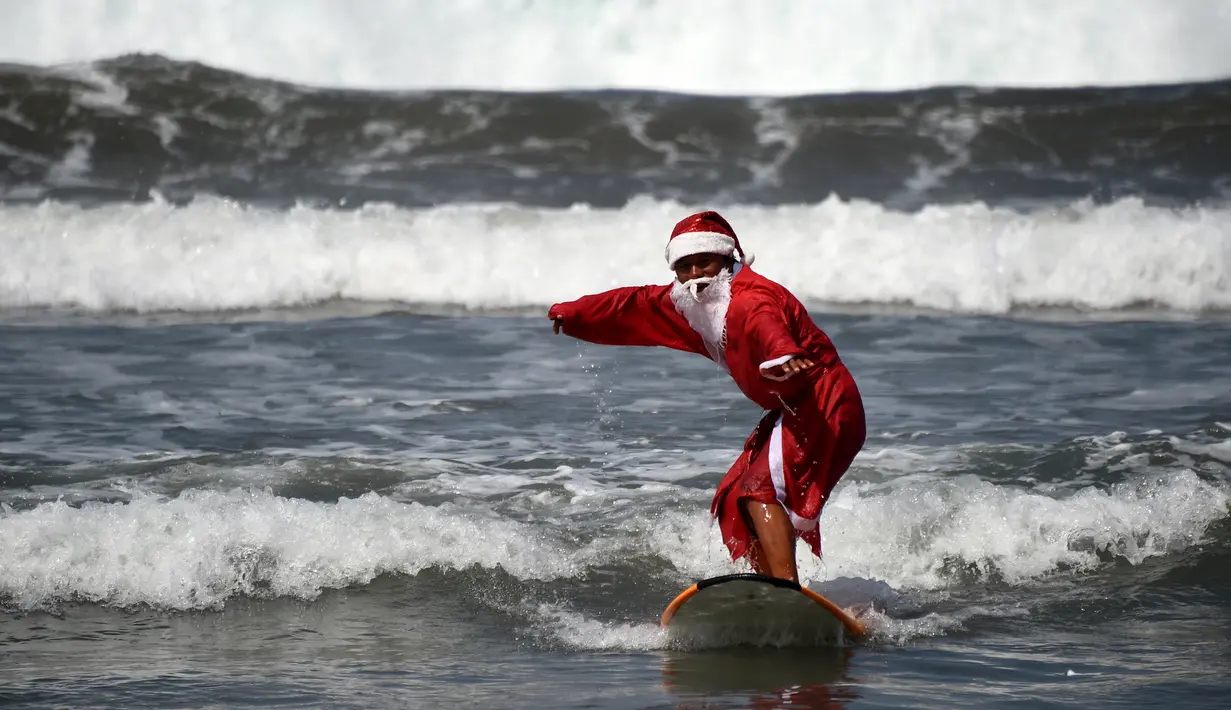 Seorang pria berkostum Santa Claus berselancar di Pantai Kuta, Bali, Senin (10/12). Setiap tahunnya, ribuan wisatawan mendatangi Bali saat menjelang natal dan tahun baru. (AFP PHOTO / Sonny Tumbelaka)