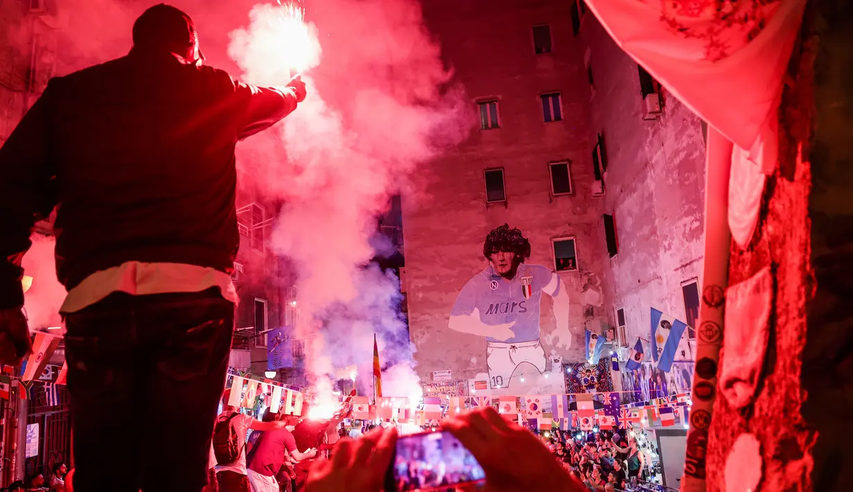 Orang-orang menyalakan suar saat mereka berkumpul di depan mural raksasa Diego Maradona untuk memberi penghormatan dan memperingati mendiang legenda sepak bola di hari ulang tahunnya di Naples, Italia, 30 Oktober 2022. Legenda sepak bola asal Argentina, Diego Armando Maradona yang lahir pada 30 Oktober 1960 meninggal pada 25 November 2020. (Alessandro Garofalo/LaPresse via AP)