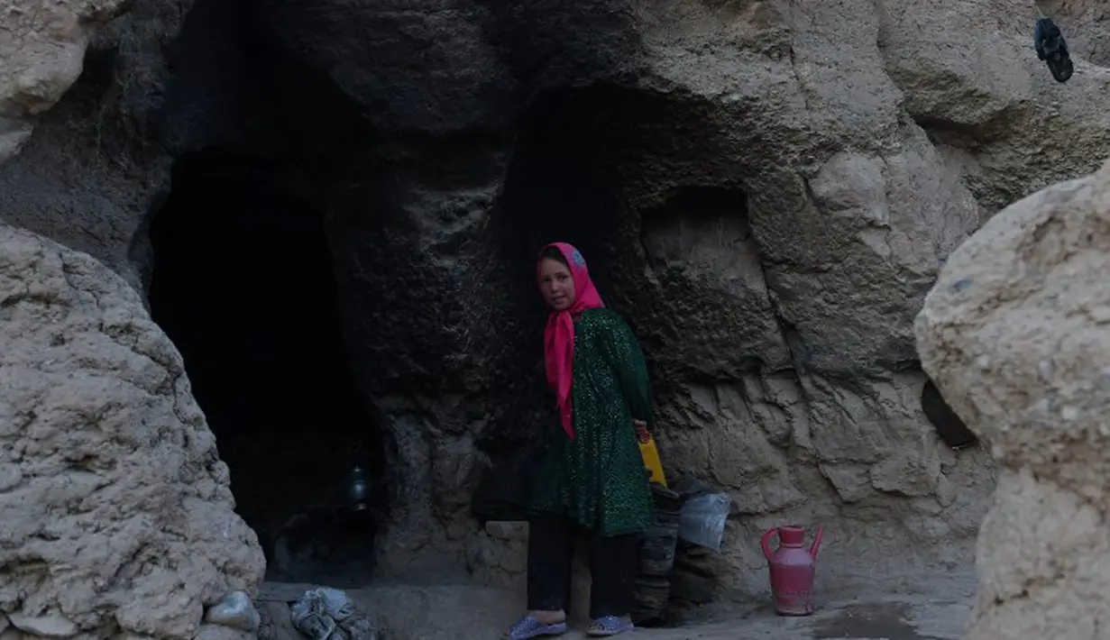 Seorang gadis kecil berdiri di pintu masuk gua di kota Bamiyan, Kabul. Foto diambil pada 19 Juni 2015. Ratusan warga miskin Afghanistan terpaksa menghuni gua-gua tersebut untuk dijadikan rumah karena tak memiliki tempat tinggal. (AFP PHOTO / SHAH Marai)