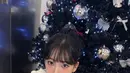 Karina aespa berfoto di pohon Natal dengan ornamen silver. Ia tampil mengenakan knit top putih cut out di bagian merah dipadukan rok panjang tartan. [@katarinabluu]