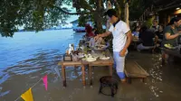 Pelanggan Chaopraya Antique Café di tepi sungai menikmati ketinggian air di Sungai Chao Phraya dekat Bangkok, Thailand, Kamis (7/10/2021). Karena kebanjiran, alih-alih kursi kosong dan meja kosong justru restoran penuh seperti biasanya bagi para pencinta santapan 'hot-pot'. (AP Photo/Sakchai Lalit)