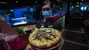 Seorang pekerja menunjukkan pizza dengan daun ganja di sebuah restoran di Bangkok, Thailand pada 24 November 2021. Pelanggan juga dapat memilih topping sesuai keinginan mereka, dengan biaya tambahan 100 baht atau Rp42 ribu untuk dua atau tiga lembar daun ganja. (AP Photo/Sakchai Lalit)