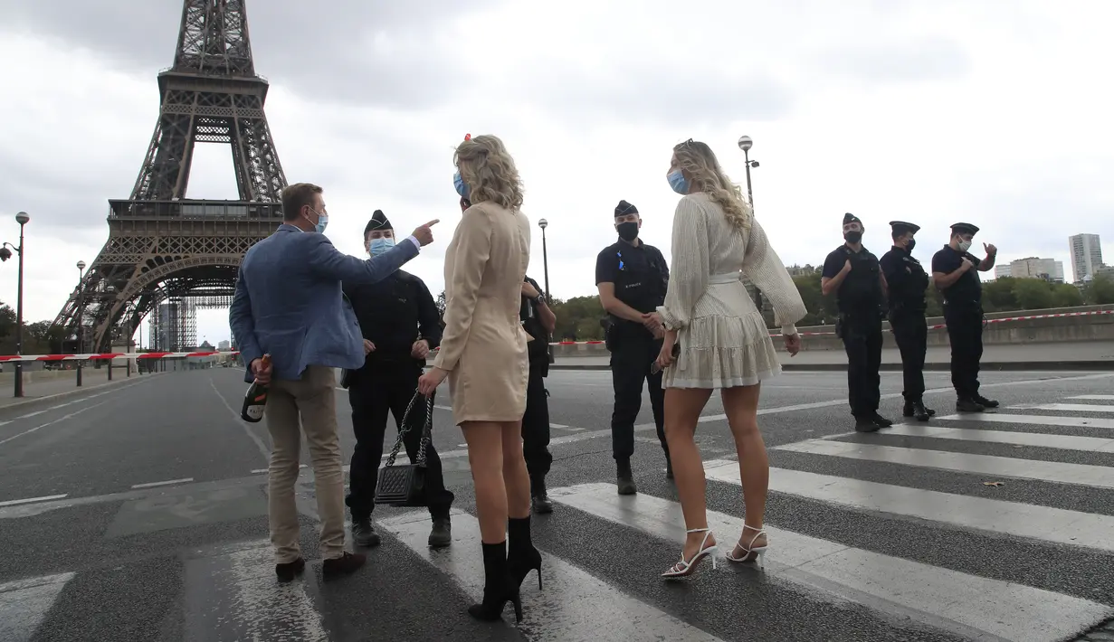 Turis Rusia, salah satunya memegang sebotol sampanye, berbincang dengan petugas polisi yang mengamankan jembatan menuju Menara Eiffel di Paris, Rabu (23/9/2020). Polisi Paris telah memblokir daerah sekitar Menara Eiffel setelah ancaman bom telepon. (AP Photo / Michel Euler)