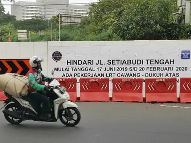 Pengendara sepeda motor melintas dekat proyek pembangunan jalur kereta Light Rail Transit (LRT) di Jalan Setiabudi Tengah, Jakarta, Senin (17/6/2019). Jalan Setiabudi Tengah ditutup mulai 17 Juni 2019 hingga 20 Februari 2020. (Liputan6.com/Herman Zakharia)