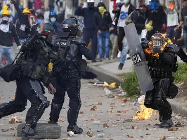 Sejumlah polisi berlari untuk membantu rekan mereka yang terkena bom molotov saat protes antipemerintah di Bogota, Kolombia, Senin (28/6/2021). Protes dipicu oleh usulan kenaikan pajak atas layanan publik, bahan bakar, upah dan pensiun. (AP Photo/Fernando Vergara)