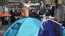 Seorang tunawisma mengenakan pakaian di depan tenda yang didirikannya di kawasan Martin Place, pusat kota Sydney, Rabu (9/8). Di perkampungan tenda para tunawisma itu mereka bertahan hidup dengan membuka lapak di pinggir jalan. (PETER PARKS / AFP)