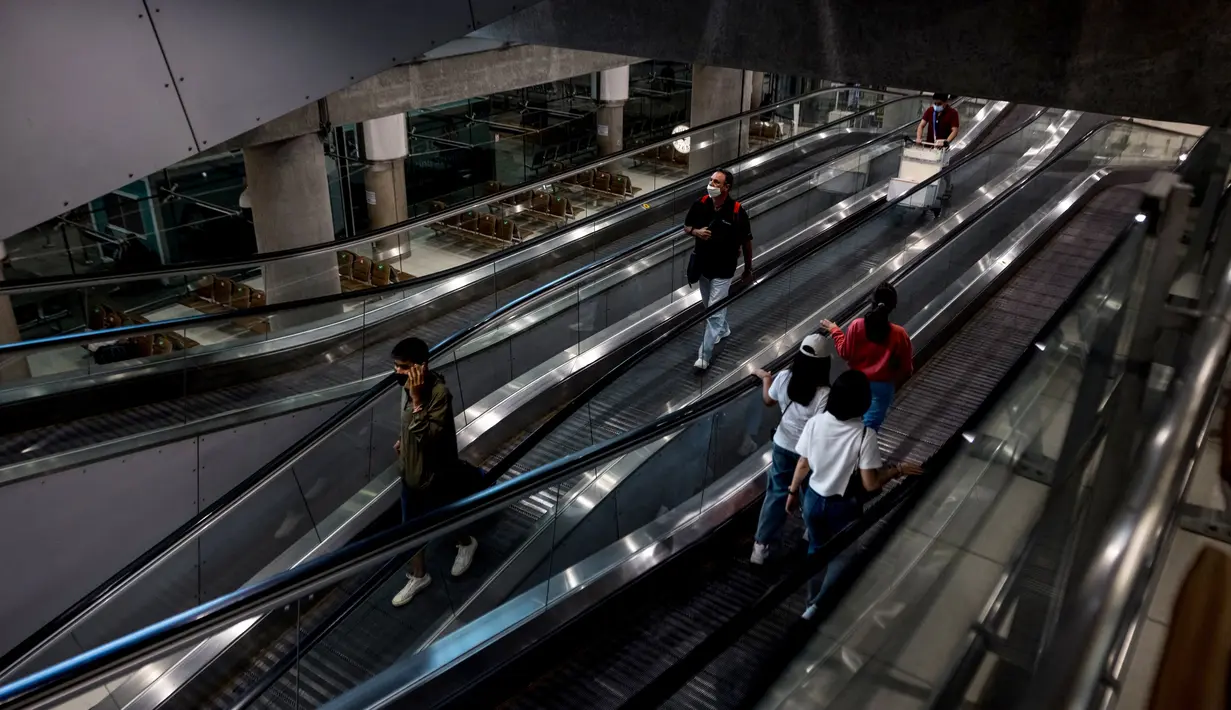 Orang-orang menaiki eskalator di Bandara Suvarnabhumi di Bangkok, saat Thailand melanjutkan skema perjalanan bebas karantina untuk pelancong yang divaksinasi, Selasa (1/2/2022). Program ini sebelumnya ditangguhkan karena melonjaknya kasus Covid-19 di Thailand. (Jack TAYLOR/AFP)