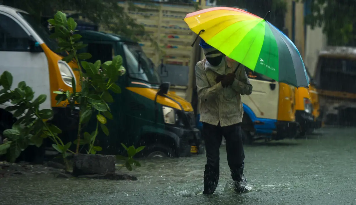 Seorang pria berjalan di sepanjang jalan yang banjir di bawah hujan lebat di Chennai saat topan Nivar mendekati pantai tenggara negara itu, (25/11/2020). (AFP/Arun Sankar)