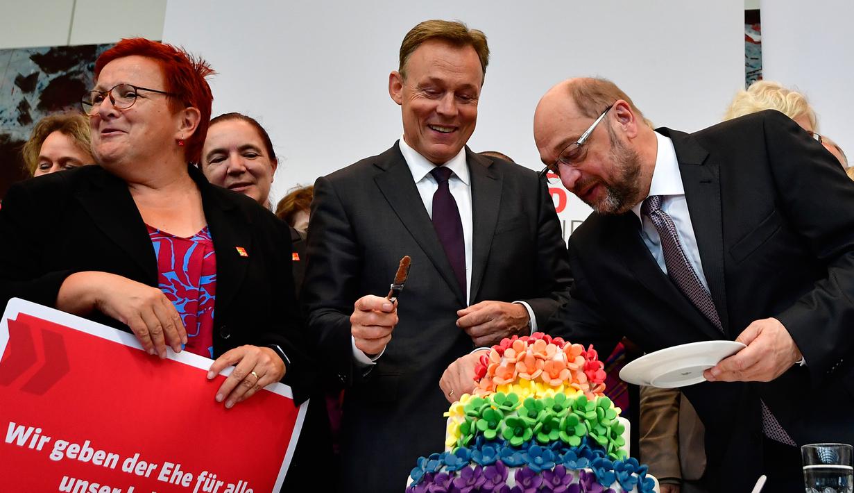 Pemimpin kelompok parlementer partai SPD, Thomas Oppermann (tengah) bersama Martin Schulz memotong kue pengantin dengan warna pelangi dan dihiasi patung-patung dua wanita dan dua pria di Bundestag di Berlin (30/6). (AFP Photo/Tobias Schwarz)