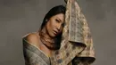 Anggun mengenakan kain tenun motif kotak-kotak warna turangga dengan bagian tepi berisi kombinasi garis miring menyerupai segitiga yang membingkai belah ketupat. Riasan natural dan rambut hitam tergerai mempercantik penampilan sang diva. Kalung bulan sabit berwarna tembaga bertengger di leher. Tangan kanan Anggun mengangkat ujung salah satu kain. (Foto: Dok. Instagram @anggun_cipta)