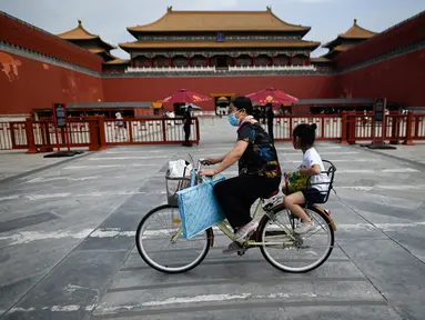Seorang perempuan mengendarai sepedanya dengan seorang anak duduk di kursi belakang melewati Kota Terlarang di Beijing, China, Selasa (7/6/2022). Pemerintah melonggarkan beberapa pembatasan Covid-19 dengan sebagian besar museum gedung bioskop, dan pusat kebugaran diizinkan beroperasi hingga 75 persen dari kapasitas. (WANG Zhao / AFP)