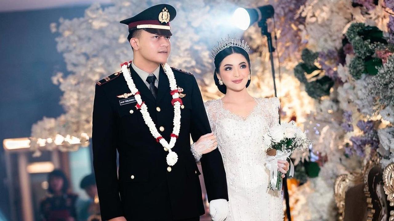 Sang mempelai pria nampak berbusana seragam dinas, sementara itu sang wanita tampil cantik dalam busana pengantin berupa dress putih panjang lengkap dengan mahkota.&nbsp;