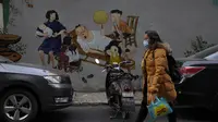 Seorang warga bermasker melewati mural yang menggambarkan kehidupan rumah tangga yang indah di Wuhan di provinsi Hubei, China, Jumat (15/1/2021). Selain masker, orang-orang menjalani kehidupan sehari-hari mereka seperti sebelumnya di kota pertama kali virus corona terdeteksi. (AP Photo/Ng Han Guan)