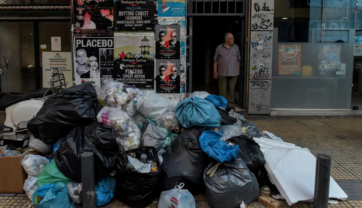 Seorang pria berdiri di belakang tumpukan sampah di pusat kota Athena, Kamis (22/6). Tumpukan sampah tampak menggunung di beberapa kota di Yunani sejak awal pekan ini setelah ribuan petugas pengumpul sampah melakukan mogok kerja. (ELEFTHERIOS ELIS/AFP)
