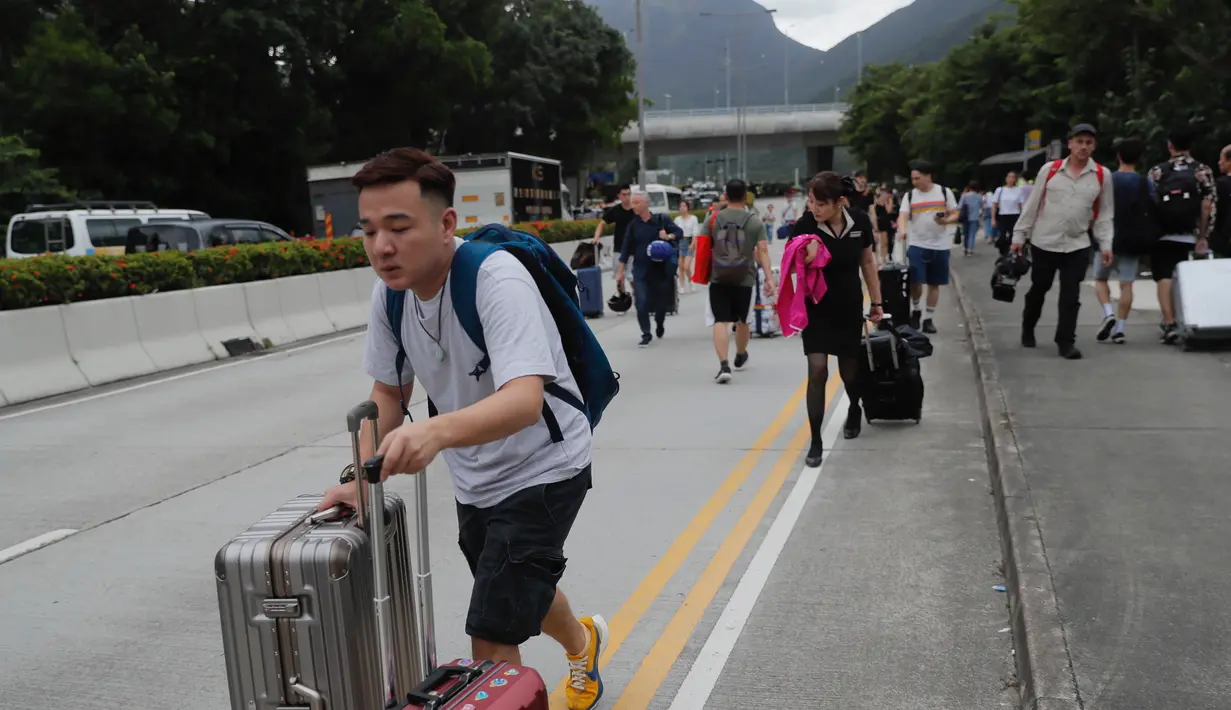 Penumpang berjalan kaki ke bandara ketika pemrotes pro-demokrasi memblokir jalan di luar bandara di Hong Kong (1/9/2019). Demonstran pro-demokrasi penentang RUU Ekstradisi kembali menjadikan bandara sebagai tempat aksi demo. (AP Photo/Kin Cheung)