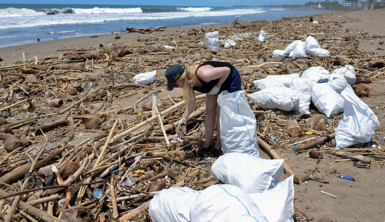 Seorang turis asing mengumpulkan sampah di antara tumpukan puing di pantai di Batu Belig di Kabupaten Badung setelah hanyut menyusul badai lepas pantai di Bali (14/12/2021). (AFP/Sony Tumbelaka)