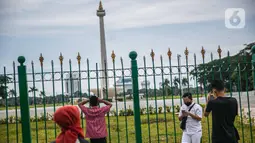 Warga berfoto di belakang Monumen Nasional atau Monas di Jakarta, Jumat (1/1/2021). Kebijakan ini bertujuan untuk mengurangi kerumunan massa di sejumlah objek wisata saat libur Tahun Baru di Jakarta. (Liputan6.com/Faizal Fanani)