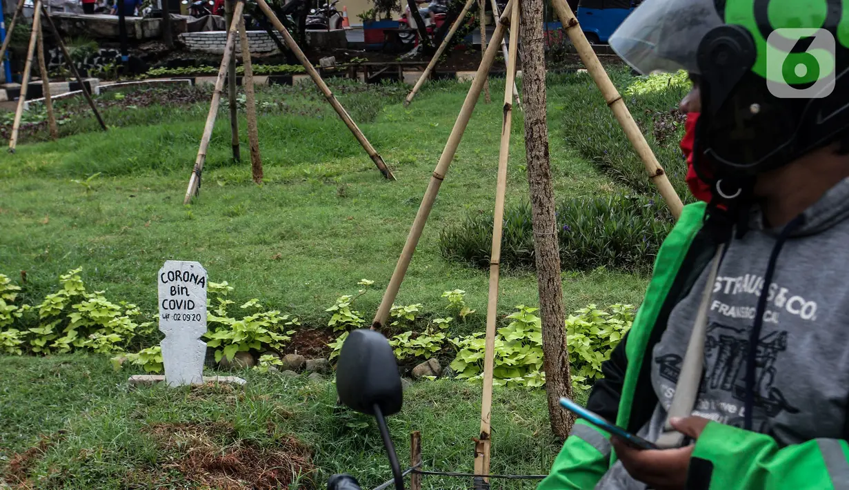 Warga melihat kuburan dengan papan nisan bertuliskan Corona bin Covid di taman Jalan Jatinegara Barat, Jakarta, Minggu (20/9/2020). Kuburan tersebut sengaja dibuat untuk mengingatkan masyarakat yang melintas akan bahaya virus Covid-19. (Liputan6.comm/Johan Tallo)