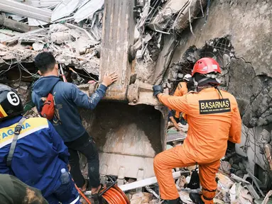 Petugas Basarnas mencari korban di reruntuhan bangunan yang rusak di Mamuju, Sulawesi Barat, Sabtu (16/1/2021). Jalan dan jembatan yang rusak, pemadaman listrik, dan kurangnya alat berat menghambat evakuasi setelah gempa bermagnitudo 6,2 SR yang melanda Majene- Mamuju. (AP Photo/ Sadly Ashari Said)